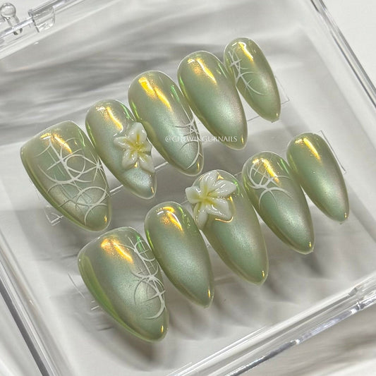 Set of green cat eye nail art designs with floral patterns in a clear case.