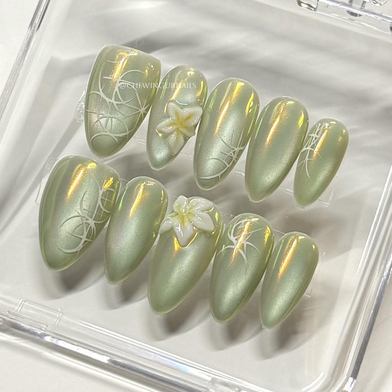 Set of green cate eye press ons nail art designs with floral patterns on a clear tray.