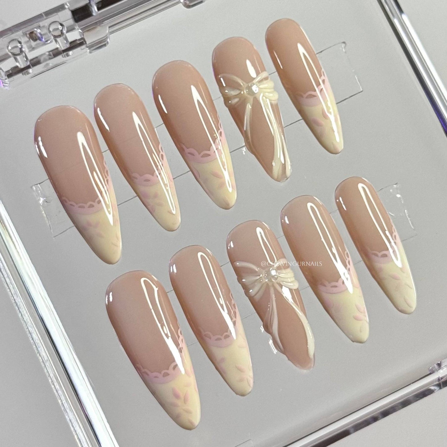 Set of beige and pink gradient nail designs with bow and flower decorations on a clear display stand.