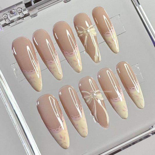 Set of beige and pink gradient nail designs with bow and flower decorations on a clear display stand.